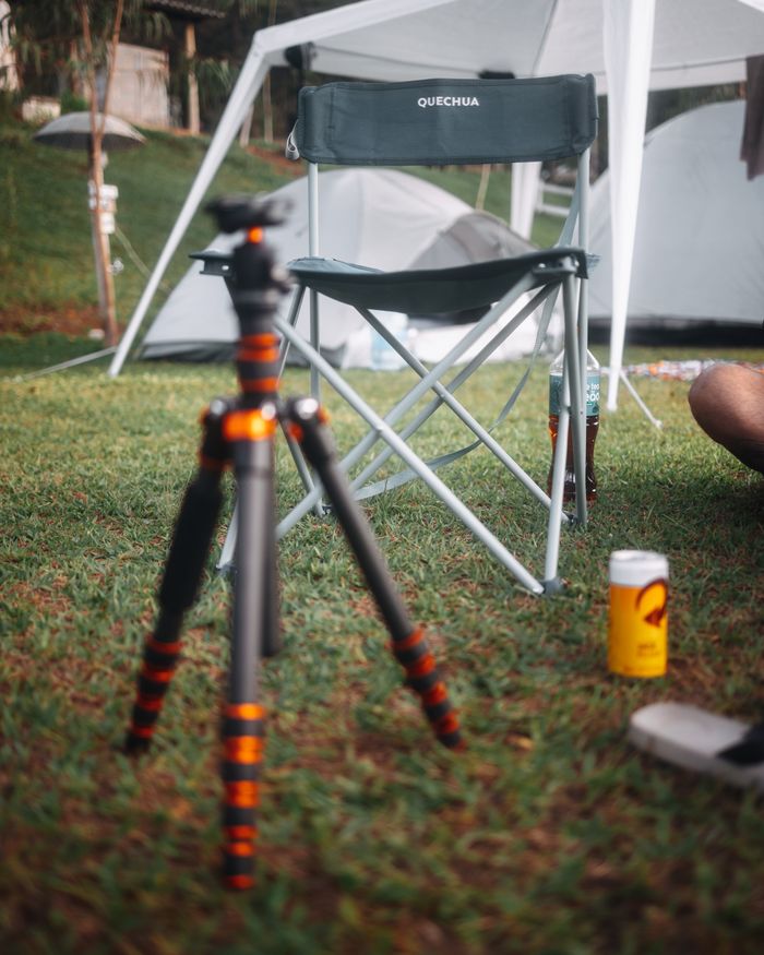 Relaxing camping scene with chair, tripod, and tent on grass.