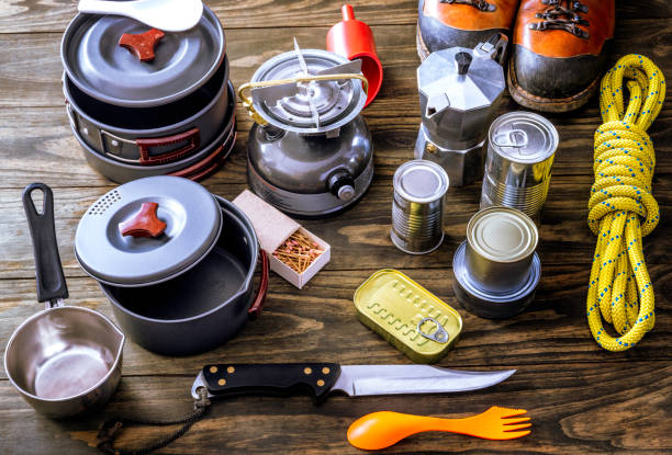 Camping cookware set with pots, pans, and utensils beside a campfire.